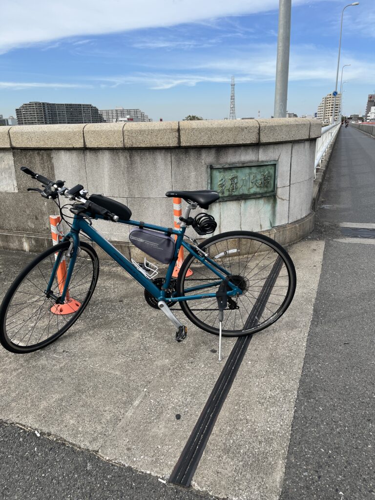 「多摩川大橋」の銘板の前に停めたクロスバイク。風をまといながら、しばしの休息。