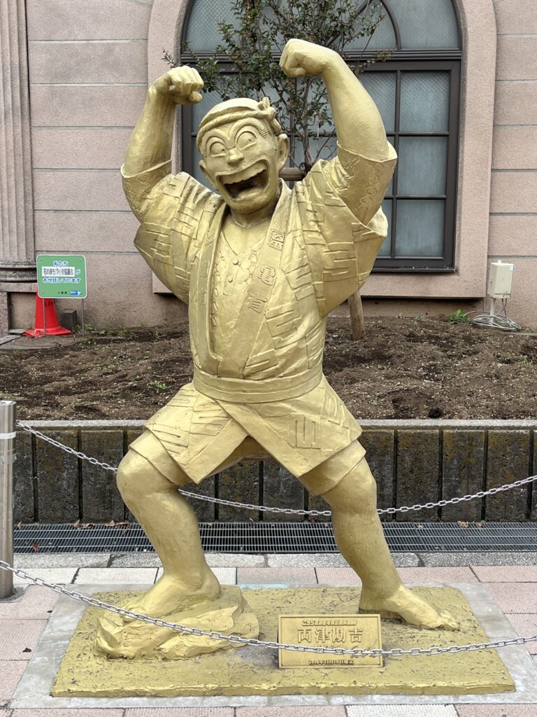 両さんの黄金像。腕を上げ、笑顔でポーズを取っている。